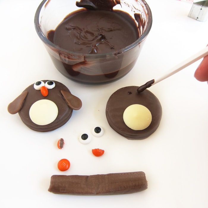 Adding drops of melted light cocoa candy melts to a penguin OREO in order to add the candy eyes.
