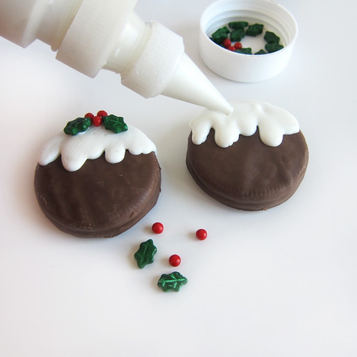piping bright white candy melts over a chocolate fudge covered OREO to make it look like Christmas pudding.