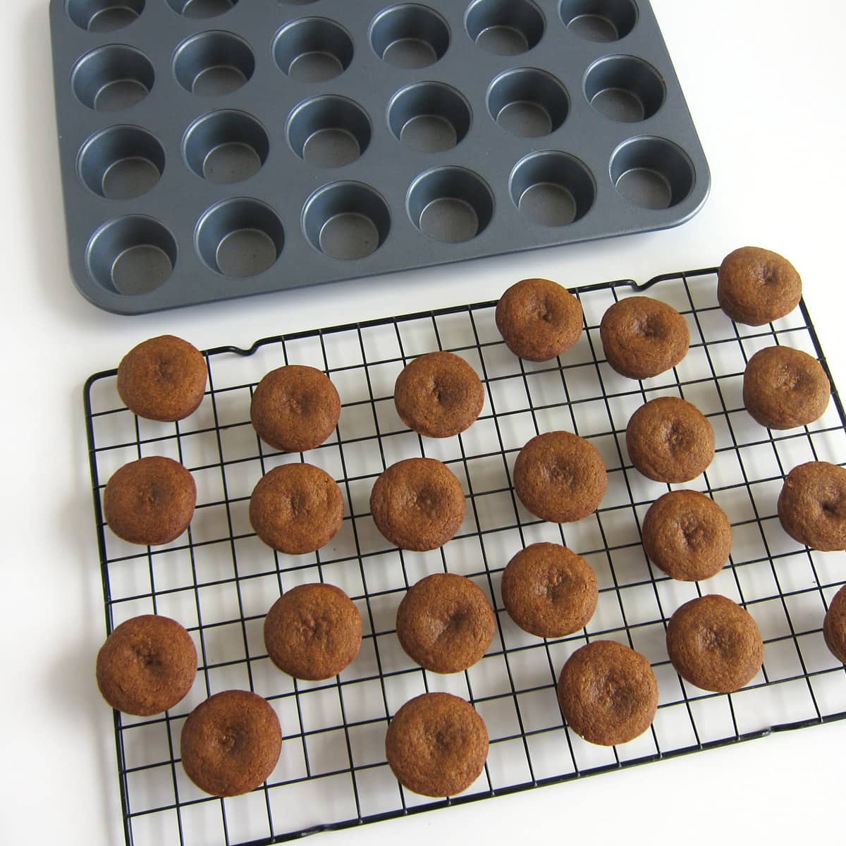 gingerbread cookie cups cooling on a metal cooling rack that is set next to a mini muffin tin.