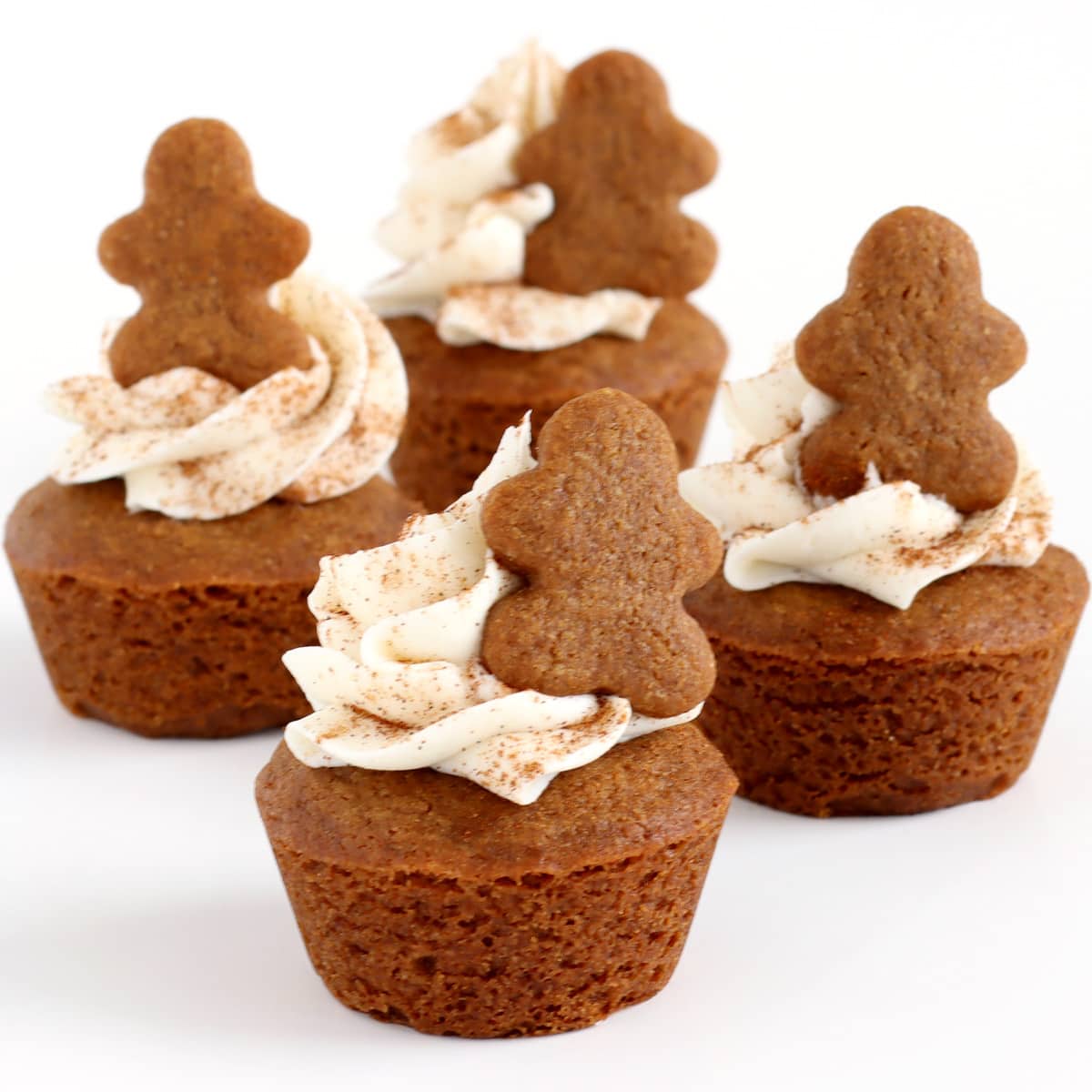 bite-size gingerbread cookie cups topped with swirls of white frosting, a sprinkling of cinnamon, and tiny gingerbread men.