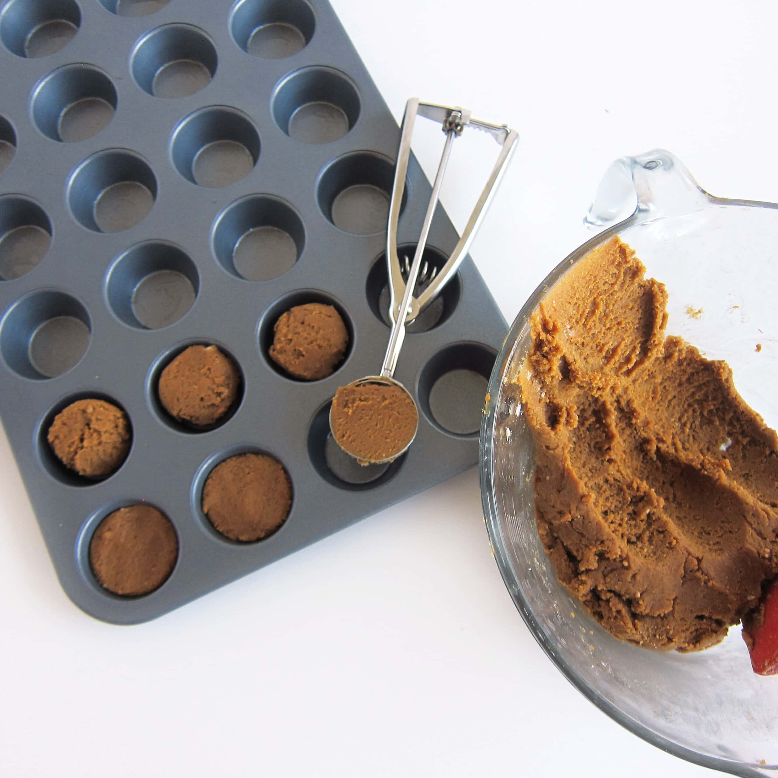 scooping balls of gingerbread cookie dough into the mini muffin tin.